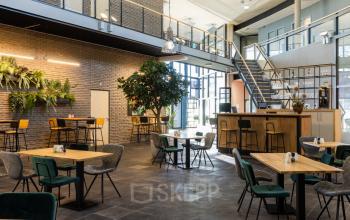 Spacious furnished office for rent at Veengang 1, Oosterwolde. Features open seating areas with plants and a staircase, ideal for office space rental.