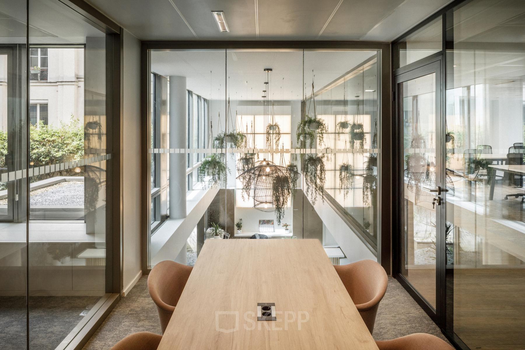 Espace lumineux dans un bureau à louer à Paris 17ème avec grande table et chaises design. Vue intérieure moderne avec verrières et plantes suspendues. Idéal pour location bureau.