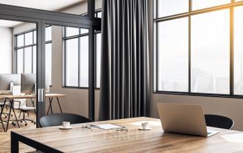 Espace de bureau à louer moderne et lumineux situé à Rue de la Bourse 12, Paris 2ème, avec une grande table en bois et des ordinateurs portables, offrant une vue captivante sur la ville.