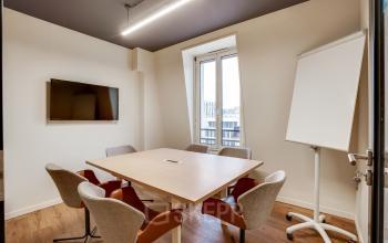 Salle de réunion moderne à Paris 2ème, idéale pour location de bureau, avec écran mural, table en bois et chaises confortables.