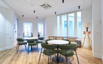 Espace de bureau à louer à rue Auber 12, Paris 9ème avec tables, chaises vertes, sol en bois et grandes fenêtres lumineuses.