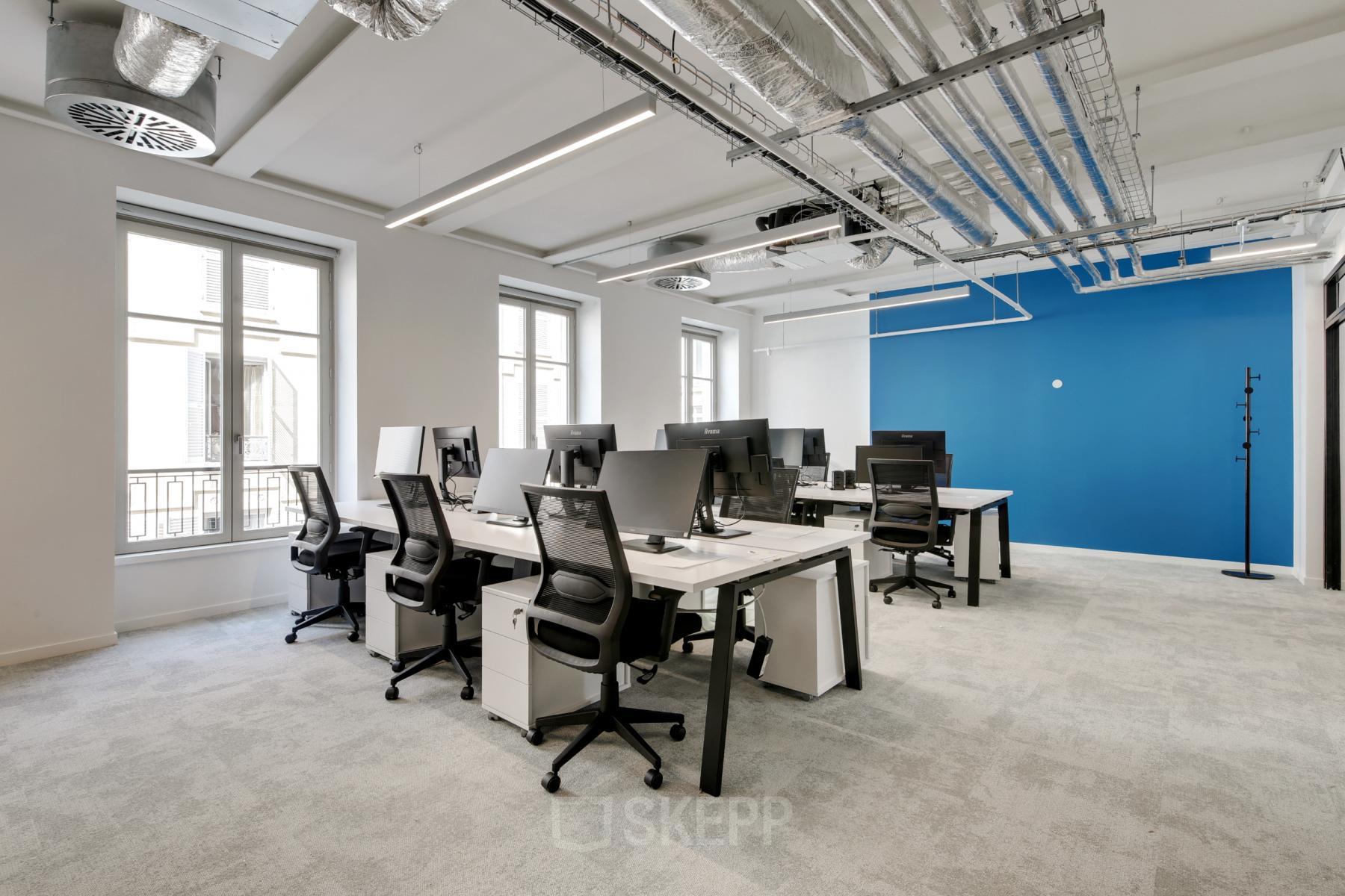 Espace de bureau à louer lumineux et moderne à rue de Provence 49, Paris 9ème, avec des bureaux équipés de chaises noires et de moniteurs.