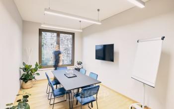 Moderner Besprechungsraum mit großem Tisch, Stühlen und TV-Bildschirm. Ein Mann bewegt sich im Raum. Perfekt zum Büroraum mieten in Potsdam Am Neuen Markt 9e.