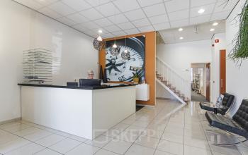Reception area of an office to rent at Leeghwaterstraat 25, Reeuwijk, featuring a modern desk with a person attending to business activities.