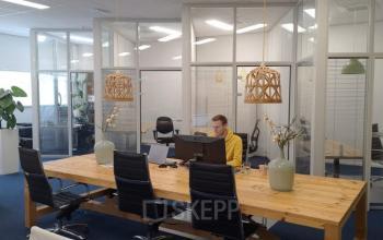 Office space rental at Leeghwaterstraat 25, Reeuwijk, featuring a spacious, glass-walled interior with wooden tables and modern chairs, where a person is working at a desk.