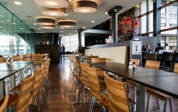 Bright office cafeteria space with wooden chairs and tables at Ericssonstraat 2, Rijen. Multiple people are engaging in business activities.