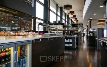 Modern pantry area with large windows, dark wooden counters, and various food and beverage offerings in an office building at Ericssonstraat 2, Rijen.