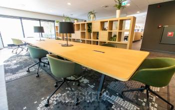 Furnished office space with green chairs and a long wooden table, ideal for office space rental at Laan van Vredenoord 33, Rijswijk.