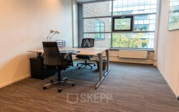Furnished office space available for rent at Laan van Vredenoord 33, Rijswijk, featuring a desk, chairs, and large window with natural light.