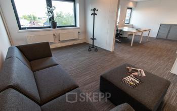 Bright office space for rent at Laan van Vredenoord 33, Rijswijk, featuring a cozy seating area and a work desk near a window with a view.