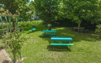 Outdoor seating area with several green picnic tables surrounded by trees at Lange Kleiweg 50-62, ideal for breaks or informal meetings when renting office space.