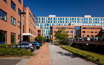 Exterior view of the office buildings at Lange Kleiweg 50-62, Rijswijk. The modern architecture features red brick and glass facades, with a pathway and parked cars in the foreground. Ideal for office space rental.