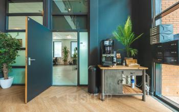 Spacious interior entrance of an office building on Lange Kleiweg in Rijswijk, featuring wooden floors, potted plants, and a coffee station. Ideal for office space rental seekers.