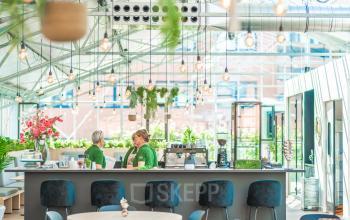 Modern office space rental at Lange Kleiweg 50-62, Rijswijk, featuring a bright and open interior with lush greenery. Two people prepare coffee at a sleek counter bar, enhancing the welcoming atmosphere.