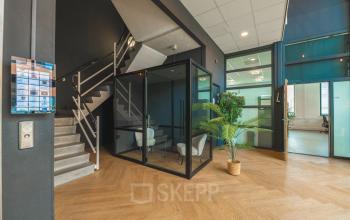 Modern office interior at Lange Kleiweg 50-62 in Rijswijk, featuring a glass-walled meeting pod, wooden flooring, and a staircase. Ideal office space rental with a contemporary design and flexible workspace options.