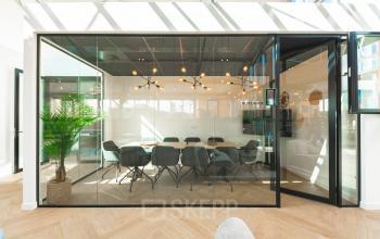 Modern conference room at Lange Kleiweg office, Rijswijk, featuring a large glass wall, contemporary lighting, and a long table with chairs. Ideal office space rental for meetings.