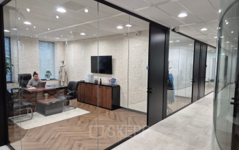 Interior view of a modern office to rent at Laan van Zuid Hoorn 70, Rijswijk, showcasing a meeting room with glass walls, wooden flooring, and office furniture including a desk and chairs.