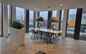 Modern office space with a large table, chairs, and overhead lighting, set near expansive windows, perfect for meetings or collaborative work. Ideal for office space rental in Rijswijk.