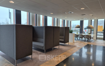 Modern office space with stylish seating and a conference table, featuring large windows letting in natural light, located at Laan van Zuid Hoorn 70, Rijswijk. Ideal office space rental with a contemporary design.