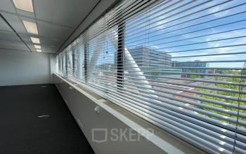 Spacious office interior with large windows and a view of Rijswijk's skyline, showcasing empty floor space ready for office space rental.