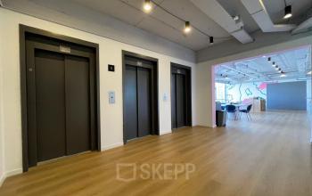 Spacious and modern office entrance at Generaal Eisenhowerplein 111 111, Rijswijk, featuring wooden flooring, elevators, and creative lighting, ideal for office space rental.
