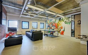Spacious office to rent with modern furnishings, featuring a playful mural and a ping pong table, situated at Patrijsweg 62, Rijswijk. Ideal office space rental for creative work.