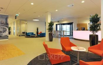 Spacious office reception area at Patrijsweg 62, Rijswijk, featuring modern decor with orange and blue seating and a sleek reception desk. Ideal for those seeking office space rental.
