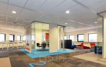 Modern workspace at Patrijsweg 4-140 in Rijswijk featuring glass-walled meeting rooms, open seating areas, and natural light through large windows, highlighting a professional office space rental opportunity.