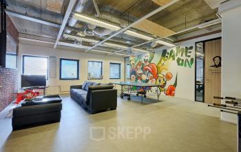 Bright office space rental at Patrijsweg 4-140 in Rijswijk featuring an open floorplan with a gray couch, table tennis setup, and a graffiti wall art.