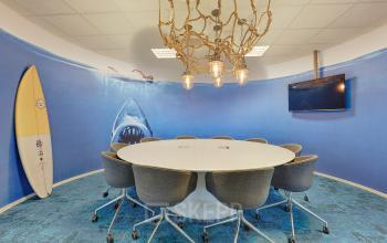 Unique conference room with a round table, modern chairs, a surfboard, and a shark mural, located at Patrijsweg 4-140, Rijswijk. Office space rental available.
