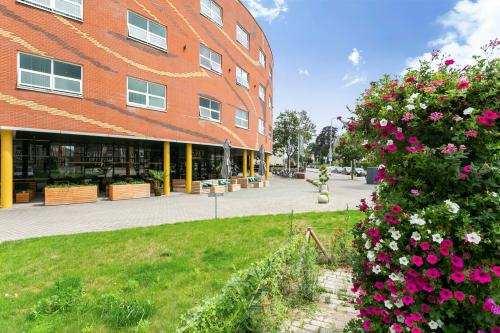 Exterior view of the office building at Kapellerpoort 1, Roermond, featuring a modern brick façade with yellow accents, and a landscaped area with flowers.
