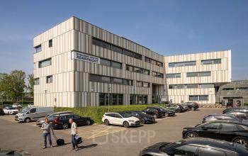 Exterior view of an office building at Boven de Wolfskuil 3, Roermond, with a parking area and two people having a conversation outside.