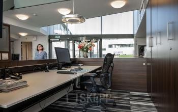 A furnished office with a desk, chair, computer, and a person entering. Ideal office space rental for professionals at Boven de Wolfskuil 3, Roermond.