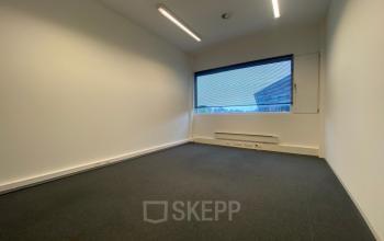 A vacant office space with carpeting and a large window, suitable for rent at Boven de Wolfskuil 3, Roermond. Ideal for businesses seeking a blank canvas for their workspace.