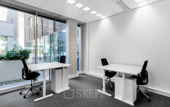 Bright office space rental at Rotterdam Airportplein 22 featuring two desks and chairs in a modern interior with large windows.