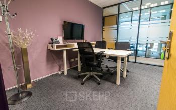 Furnished office space in Rotterdam Airport with a table, chairs, and a wall-mounted TV, ideal for rent. The glass partition adds a modern touch to this quiet and professional workspace.