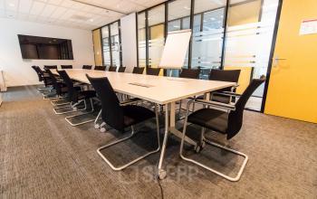 A furnished conference room at Rotterdam Airport with a long table and several chairs, ideal for office space rental.