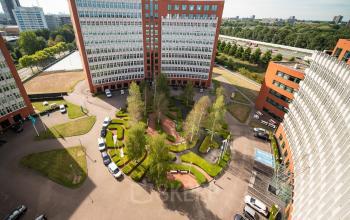 View of the office complex at George Hintzenweg 77 - 89 in Rotterdam Alexander, featuring multiple tall buildings surrounding a landscaped courtyard with neatly trimmed greenery and parked cars. Ideal office space rental location.