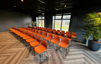 Spacious office space to rent in Rotterdam Alexander featuring rows of orange chairs facing windows with green views, perfect for meetings or presentations.