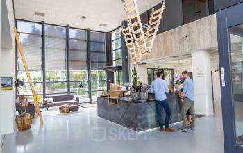 Modern office space at Marten Meesweg 8-10, Rotterdam Alexander, featuring a stylish reception area with a unique ceiling light fixture and people engaged in business activities.