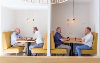 Professionals having meetings in a contemporary office space with booth seating, hanging lights, and minimalistic decor at Marten Meesweg 8-10, in Rotterdam Alexander, Rotterdam.