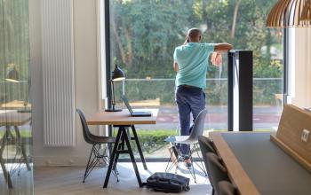 Modern workspace at Marten Meesweg 8-10, Rotterdam Alexander, with a man on a phone call near large windows and two desks equipped with laptops and chairs.