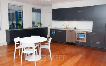 Office kitchen area at Hoofdweg 66, Rotterdam Alexander, with black cabinets, stainless steel appliances, white table and chairs, and wooden flooring.