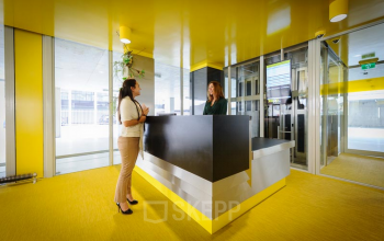 Brightly-lit reception area at Bahialaan 100, office space rental in Rotterdam Brainpark, with two professionals engaging in conversation.