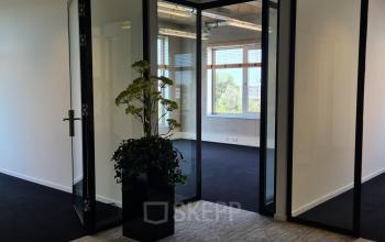 Modern office space at Bahialaan 100 in Rotterdam Brainpark featuring glass doors, black carpet, and natural light from large windows.