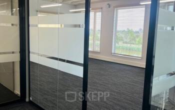 Office space available for rent at Bahialaan 100, Rotterdam Brainpark, featuring glass partition walls and carpet flooring with abundant natural light.