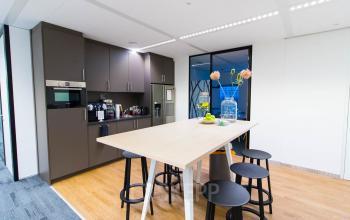 Modern office pantry at Weena 505, Rotterdam Central Station, featuring a kitchenette, tall table with stools, and vibrant decor, perfect for a quick break.