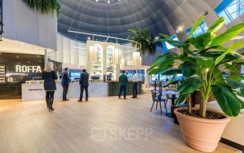 Modern office lobby at Weena 505, Rotterdam Central Station, with people engaging in business activities near reception and seating area under a domed ceiling.