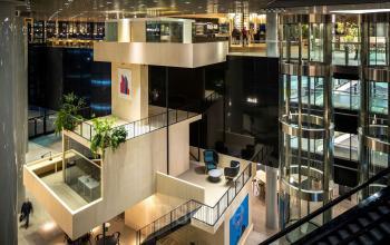 Modern interior of office building located at Weena 505, Rotterdam Central Station, featuring multi-level open workspaces with various seating areas and glass elevators. Ideal for office space rental.