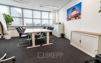 Furnished office space at Weena 290, featuring a conference table, chairs, and a large window overlooking Rotterdam Central Station. Ideal for office space rental with natural light.